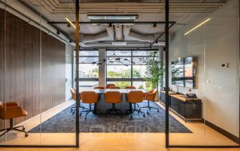 Modern furnished conference room at Zwaansvliet 1 in Amsterdam Buitenveldert, featuring a large wooden table, orange chairs, and window views, ideal for office space rental.