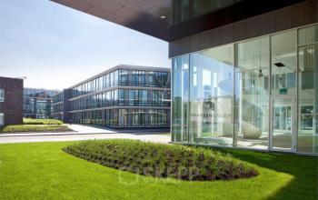 Exterior view of the modern office buildings at De Cuserstraat 91, Amsterdam Buitenveldert, showcasing large glass windows and a landscaped courtyard.
