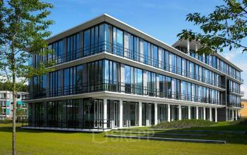 Modern office building at De Cuserstraat 85, Amsterdam Buitenveldert, available for office space rental, featuring large windows and a green lawn.