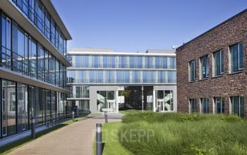Modern office building located at De Cuserstraat 85 in Amsterdam Buitenveldert, featuring large glass windows and green landscaped surroundings, ideal for office space rental.