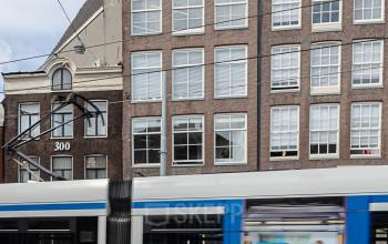 Historic brick office building at Nieuwezijds Voorburgwal 296-298 with a passing tram in Amsterdam Center.