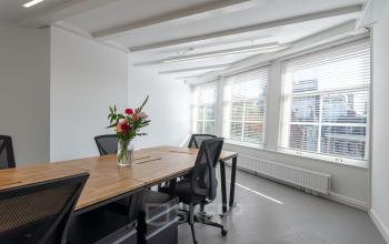 Bright office space with large windows, natural light, and wooden desks in Nieuwezijds Voorburgwal 296-298. A vase with flowers on the table adds a fresh touch.