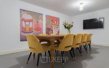 Conference room at Nieuwezijds Voorburgwal 296-298 in Amsterdam Center, featuring a long table with yellow chairs, wall art, a screen, and a vase of flowers.