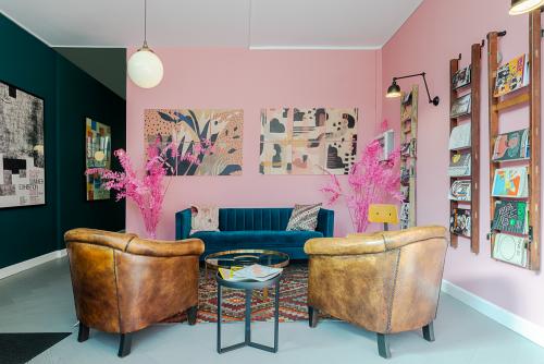 Bright, furnished lounge area with pink walls, colorful artwork, leather chairs, and a blue velvet sofa at Nieuwezijds Voorburgwal 296-298, Amsterdam Center, available for office space rental.