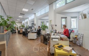 A well-lit office space rental at Oudeschans 21, Amsterdam Center, with individuals engaged in business activities at their desks.