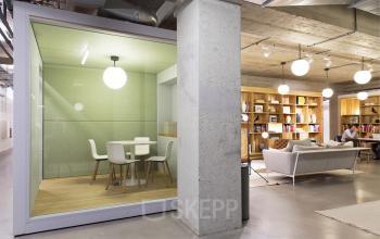 Modern office space at Vijzelstraat 68-78, Amsterdam Center, featuring a cozy meeting area with glass walls, minimalist design, and wooden shelves.