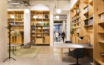 Modern office space rental at Vijzelstraat 68-78, Amsterdam Center, with wooden shelves, chic furniture, and busy professionals in a bright setting.