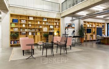 Modern office space rental at Vijzelstraat 68-78, Amsterdam Center, featuring a stylish seating area with bookshelves and plants.