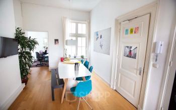 Modern office space for rent at Schippersgracht 1-3, Amsterdam Center; features stylish wooden flooring, a conference table, artwork on the walls, and a person working at a desk in the background.