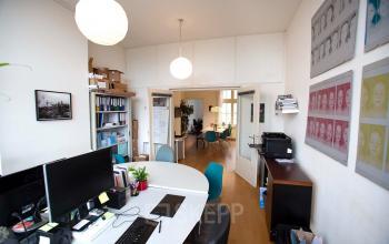 Office space at Schippersgracht 1-3 in Amsterdam Center with a round table, blue chairs, computers, and white walls decorated with art.