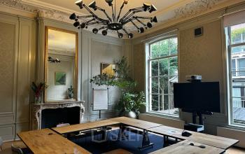 Elegant office space in Singel 126, Amsterdam Center with large windows, a stylish chandelier, and a modern U-shaped wooden desk perfect for office space rental.