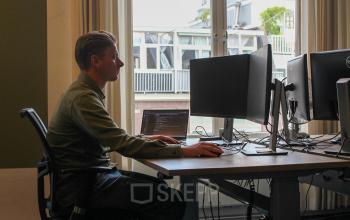 Person working at a desk in a modern office space at Singel 126, featuring multiple monitors and natural light. Ideal for office space rental in Amsterdam Center.