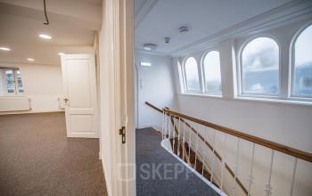 Interior view of office space for rent at Westeinde 14-16, Amsterdam Center, showcasing a carpeted area with stairway and hallway.