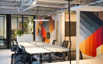 Modern office space rental at Weesperplein 4b, Amsterdam Center, featuring bright, industrial-style workspaces with colorful wall art and desks with chairs.