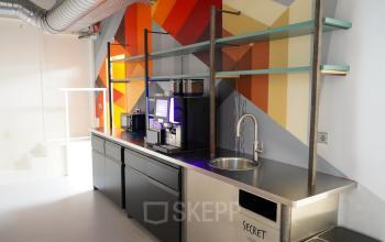 A colorful pantry area in office space rental at Weesperplein 4b, Amsterdam Center, featuring a vibrant mural, coffee machine, and industrial shelving.