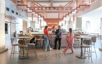 Stylish and modern office to rent at Weesperplein 4b, Amsterdam Center. People are socializing at the bar area, highlighting a unique office space rental opportunity.