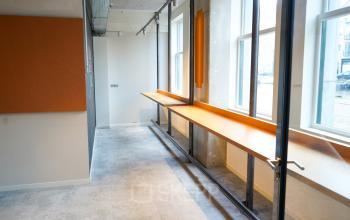Bright office space featuring large windows and a long wooden desk, available for rent at Weesperplein 4b, Amsterdam Center.