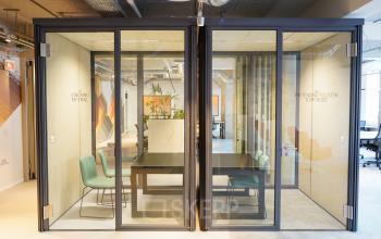 Modern office space rental at Weesperplein 4b, Amsterdam Center, featuring two small furnished meeting pods with glass walls and comfortable chairs.