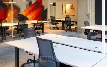 Modern office space at Weesperplein 4b, Amsterdam Center, featuring rows of sleek desks and chairs with a colorful geometric wall design, ideal for office space rental.