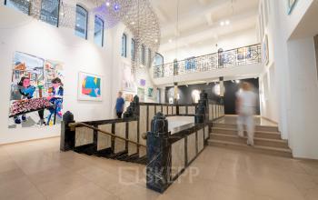 A spacious office gallery at Weesperplein 4b, Amsterdam Center, with modern art on white walls, ideal for rent office space or office space rental, featuring a mezzanine and stairs.