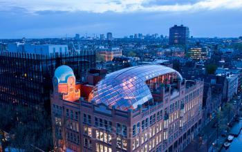 Aerial view of an office building at Weesperplein 4b, Amsterdam Center, ideal for office space rental with a distinctive glass dome roof, surrounded by cityscape.