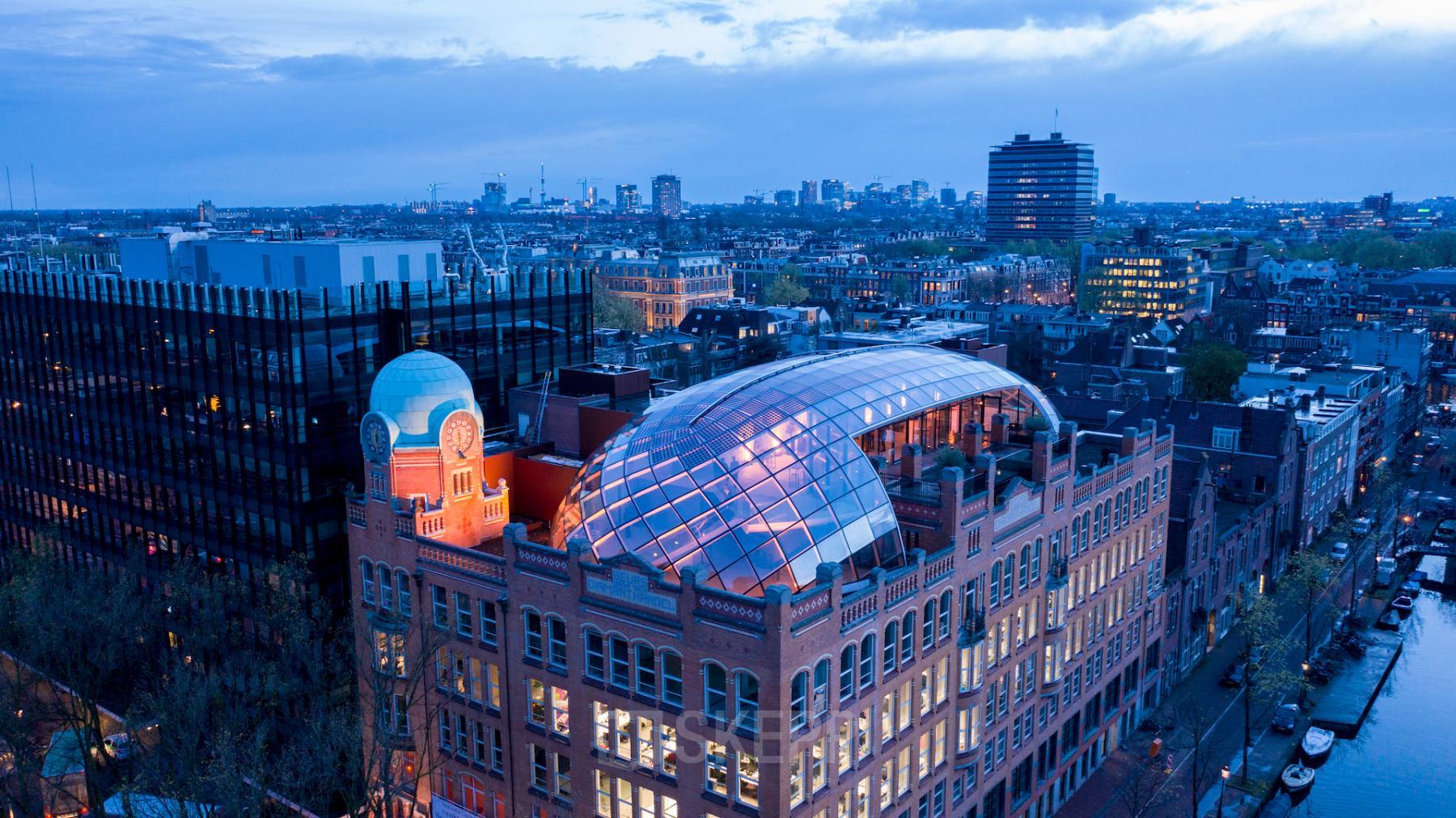 Aerial view of an office building at Weesperplein 4b, Amsterdam Center, ideal for office space rental with a distinctive glass dome roof, surrounded by cityscape.