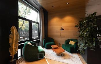 Cozy, furnished office corner at Herengracht 471, Amsterdam Center with green chairs, a small table, and a warm, wood-paneled wall. Ideal for office space rental.