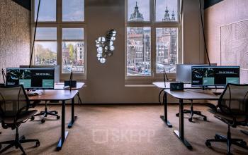 Modern furnished office space rental in Amsterdam Center at Stationsplein 9 with large windows, spacious desks, and desktop monitors.