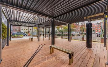 Outdoor covered space at Weesperstraat 107-121, showcasing wooden deck, benches, and a punching bag for informal meetings or breaks. Ideal for office space rental.