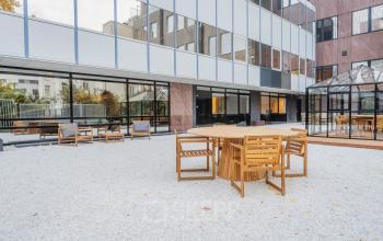 Outdoor seating area at Weesperstraat 107-121, in Amsterdam Center, featuring wooden tables and chairs, perfect for informal meetings or breaks, adjacent to the office space rental building.