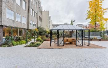 Outdoor office area with a glass-encased meeting space and surrounding greenery at Weesperstraat 107-121, Amsterdam Center, suitable for office space rental.