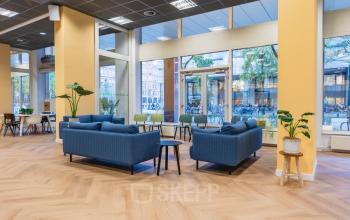 Modern office space rental at Weesperstraat 107-121 in Amsterdam featuring a stylish lounge area with blue sofas and light wood flooring, offering a welcoming environment for meetings and collaboration.