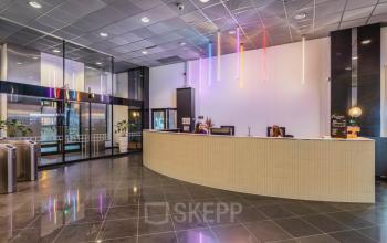Modern lobby with a sleek reception desk, illuminated by colorful hanging lights, in the office space rental at Weesperstraat 107-121, Amsterdam Center.