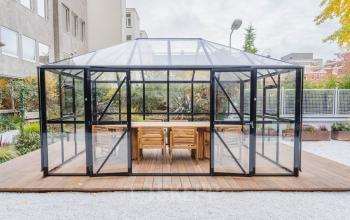 Glass-enclosed meeting space with wooden table and chairs, part of an office space rental at Weesperstraat 107-121, Amsterdam Center. Surrounded by greenery, offering a unique outdoor workspace environment.