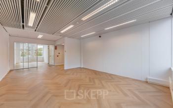 Bright, empty office space with wood-patterned floors and ceiling lights, located at Weesperstraat 107-121 in Amsterdam Center, offering ample natural light and a modern feel, ideal for businesses seeking office space rental.