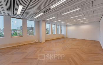 Bright office space with large windows and wooden flooring at Weesperstraat 107-121, Amsterdam Center, ideal for office space rental. The room features overhead lighting and a panoramic city view.
