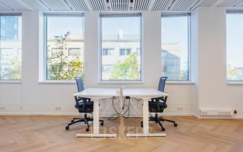 Bright office space in Amsterdam Center featuring a minimalist design with two modern desks and chairs near large windows, ideal for office space rental.