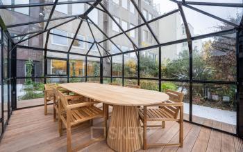 Stylish outdoor office space available for rent at Weesperstraat 107-121, Amsterdam Center. Features a modern glass enclosure with a wooden table and chairs, ideal for meetings or collaborative work.
