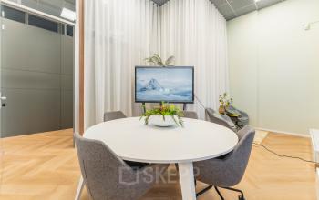 Modern office space with round table, four chairs, and a digital screen at Weesperstraat 107-121, Amsterdam Center. Ideal for small meetings or collaborative work, this furnished office offers convenient office space rental.