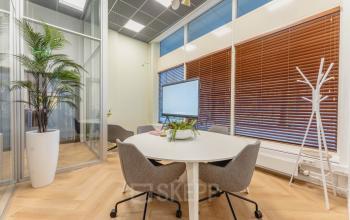 Modern office space rental in Amsterdam Center featuring a cozy meeting area with a white table, chairs, a large screen, and decorative plants.