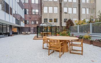 Outdoor area at Weesperstraat 107-121, Amsterdam Center, featuring wooden tables, chairs, and a modern glass enclosure ideal for informal meetings. Perfect spot for office space rental purposes.