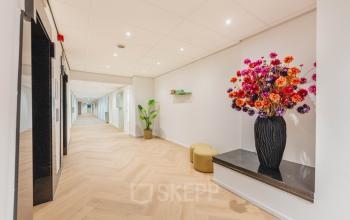 Bright hallway at Weesperstraat 107-121, Amsterdam Center, featuring wooden flooring and colorful floral decor, ideal for creating a welcoming office environment.