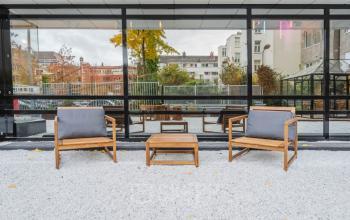 Outdoor seating area with wooden chairs and a table at Weesperstraat 107-121, Amsterdam, framed by glass windows reflecting urban surroundings. Suitable for office space rental.
