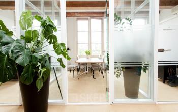 Bright office space at Keizersgracht 241, Amsterdam Center with glass-walled meeting room, large potted plants, and modern furniture.