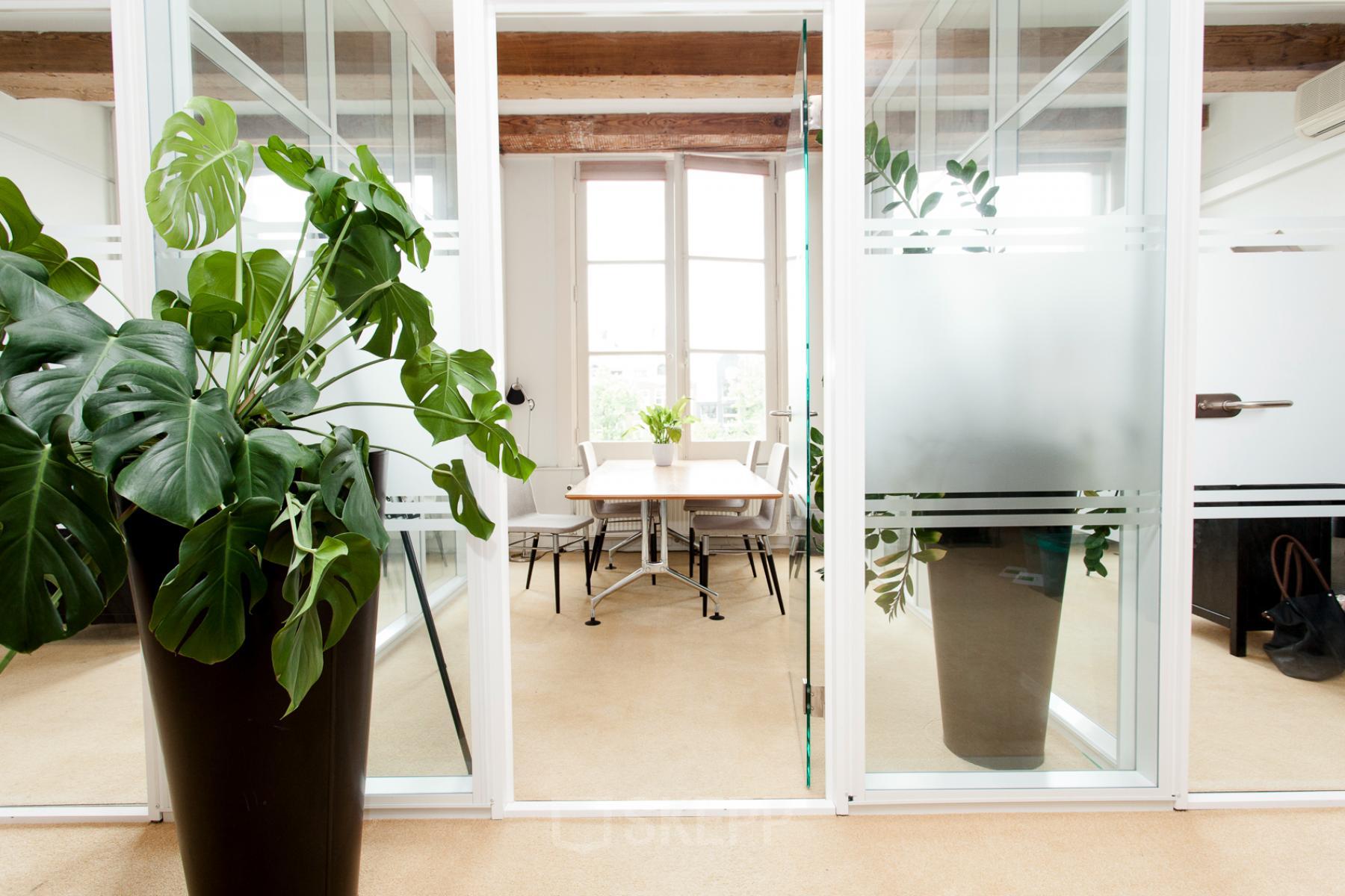 Bright office space at Keizersgracht 241, Amsterdam Center with glass-walled meeting room, large potted plants, and modern furniture.