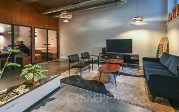 Modern lounge area in an Amsterdam office, featuring comfortable seating, stylish lighting, and a flat-screen TV, perfect for informal meetings or relaxation. Ideal office space rental opportunity at Prins Hendrikkade 48 A, Amsterdam Center.