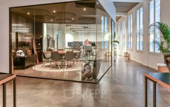 Modern workspaces at Prins Hendrikkade 48 A, Amsterdam, featuring glass-walled meeting areas and stylish furnishings, ideal for office space rental. Bright and airy with contemporary design elements.