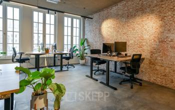 Modern office space for rent at Prins Hendrikkade 48 A, Amsterdam Center featuring an open workspace with stylish desks, functional plants, and brick walls, offering a vibrant and dynamic work environment.