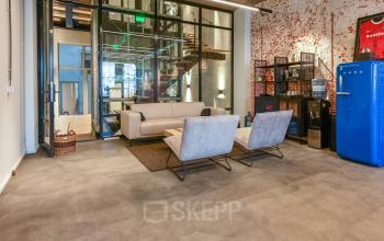 Trendy lounge area in office space rental at Prins Hendrikkade 48 A, featuring modern seating, exposed brick wall, and a retro fridge for a stylish touch.
