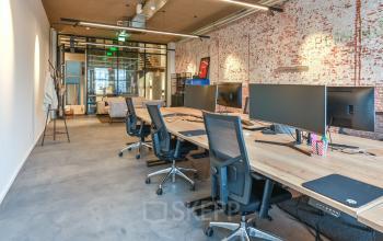 Modern office space rental at Prins Hendrikkade 48 A, featuring a sleek open floorplan with wooden desks, ergonomic chairs, and exposed brick walls, creating an inviting work environment.